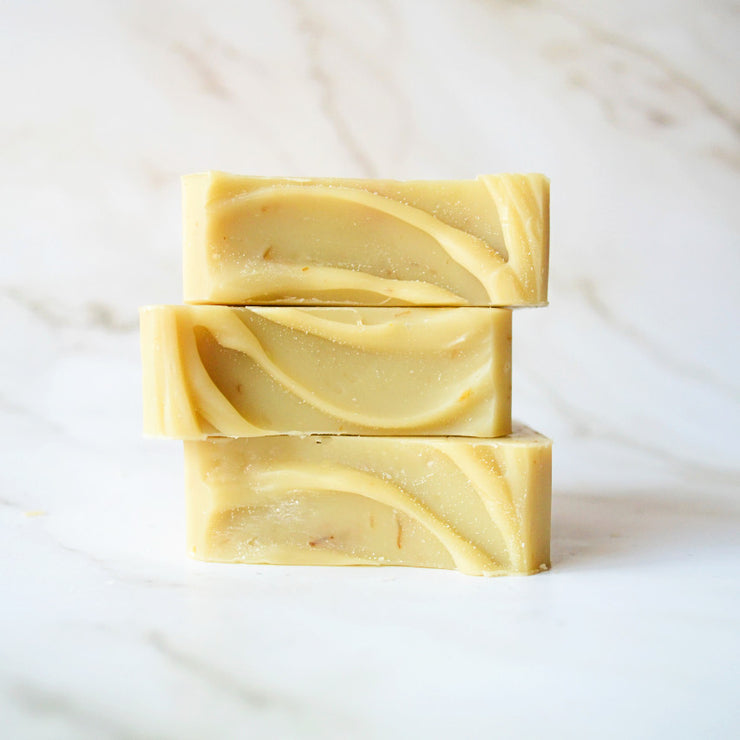 three stacked bars of lemongrass and calendula bar soap on a white marble background
